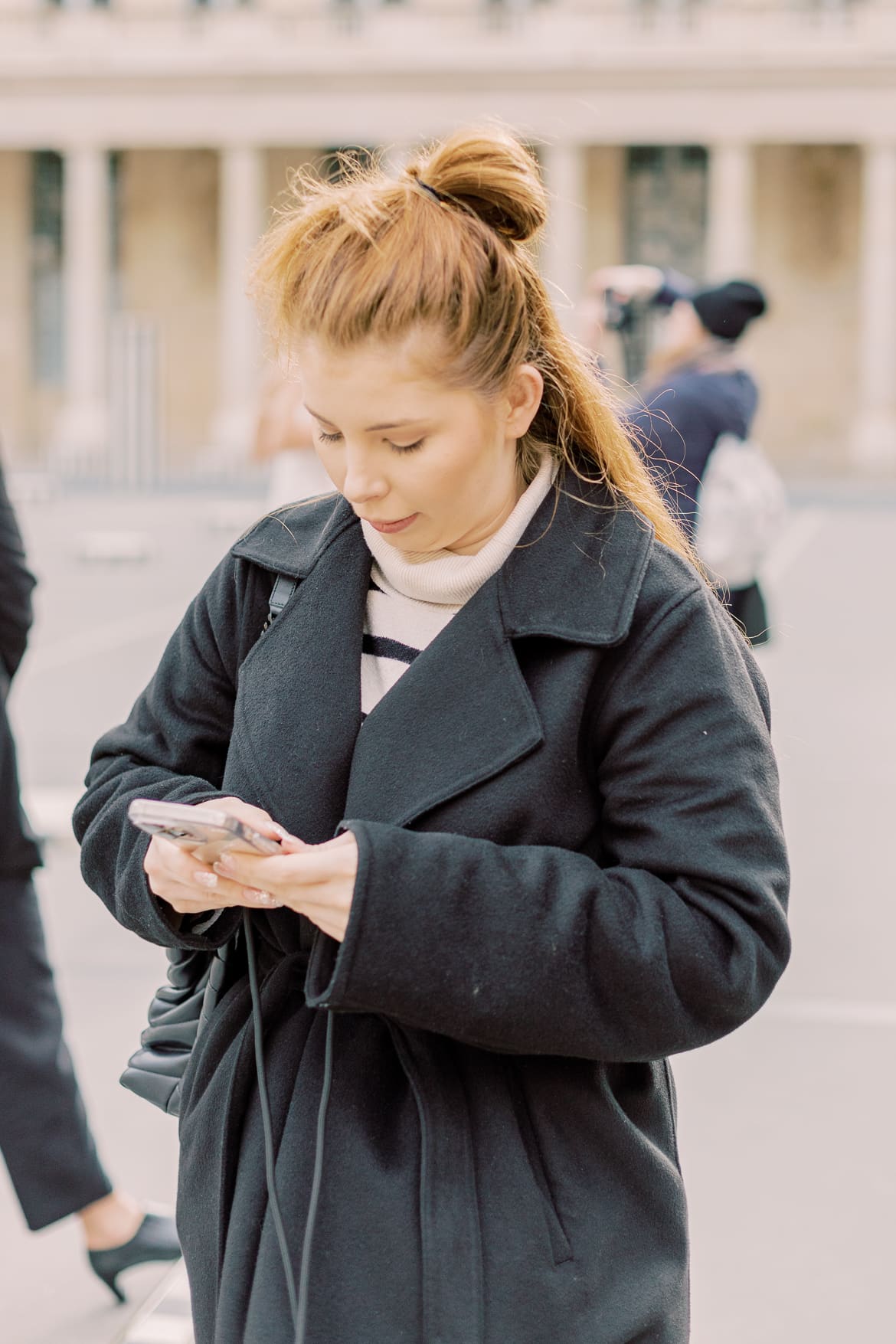 Frau im schwarzen Mantel schaut auf ihr Handy