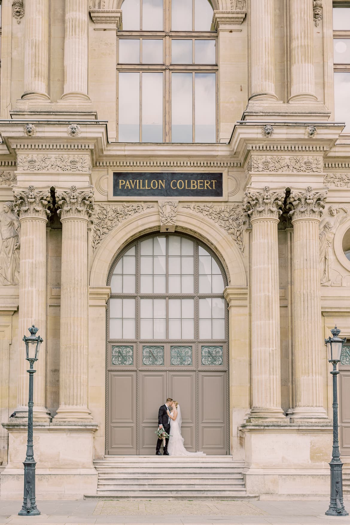 Hochzeitspaar steht vor einem riesigen Tor im Innenhof vom Louvre
