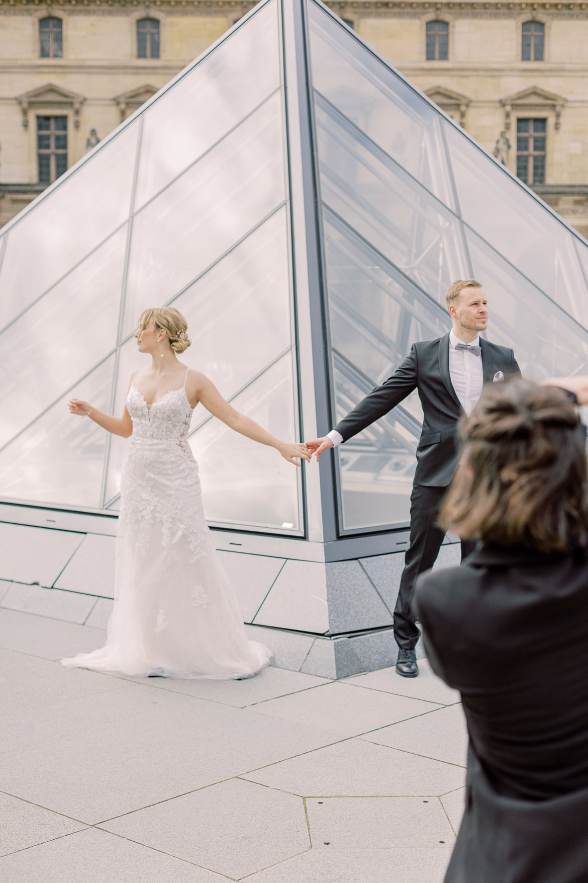 Hochzeitspaar hält sich an einer kleinen Pyramide des Louvre an der Hand, sie werden fotografiert